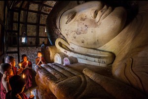 Young monks with candles worship Shin Bin Thal Yaung reclining Budddha.